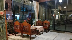Un área de estar con muebles de madera y mantel a cuadros, una puerta de cristal y una planta en maceta.