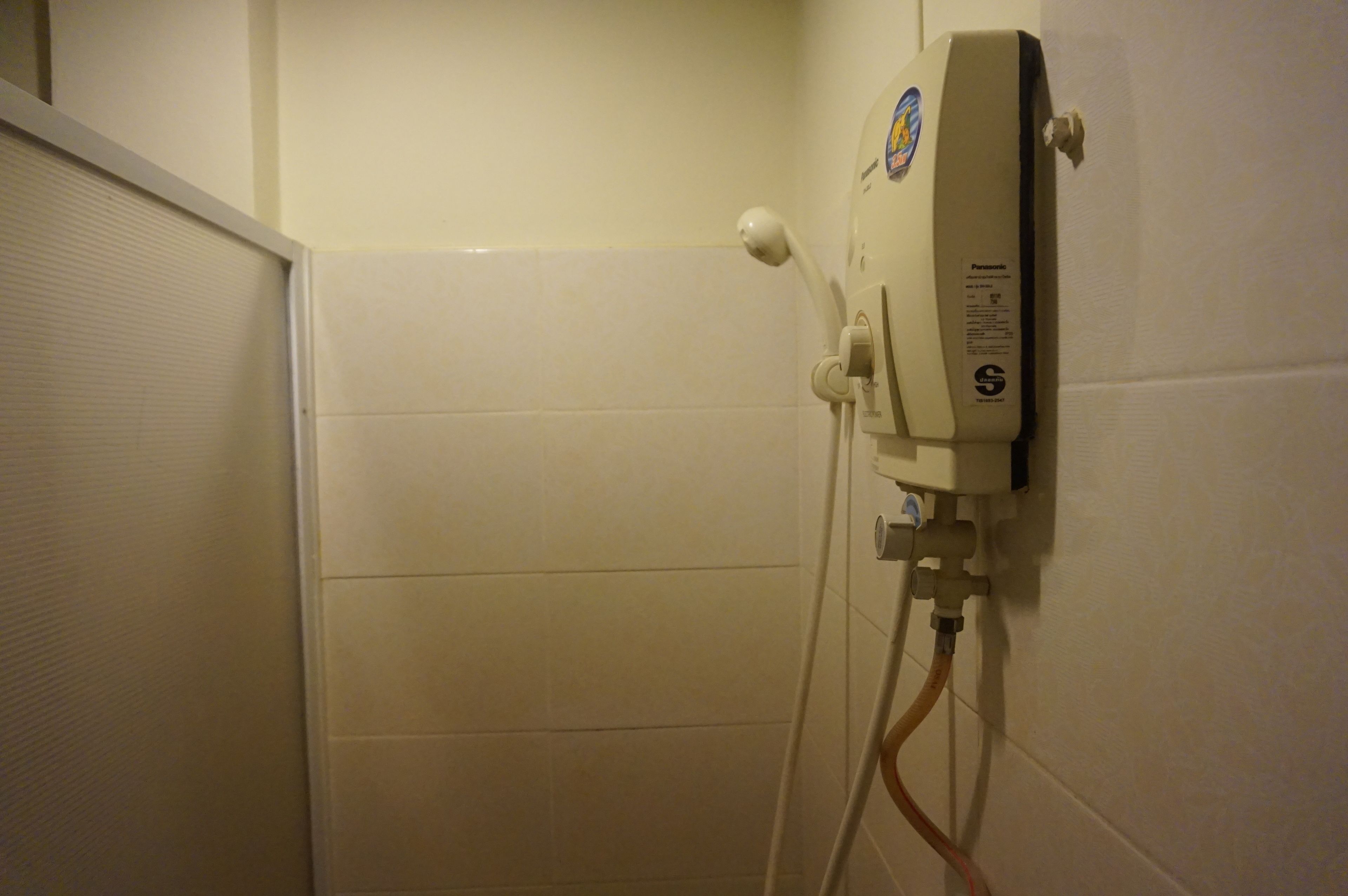 A bathroom with a wall-mounted shower unit and a door.