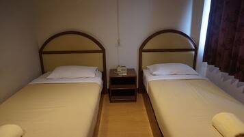Habitación de hotel con dos camas individuales, cada una con cabecero de madera y ropa de cama blanca. Entre las camas hay una mesita de noche de madera con un teléfono y un enchufe.