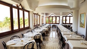 Comedor con mesas dispuestas para el servicio, ventanas amplias que dan a vistas de palmeras y un suelo estampado.