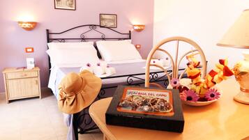 A hotel room with a bed, a nightstand, a table with a fruit arrangement, and a decorative item on the table.
