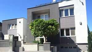 A modern two-story building with a grey facade, a large tree in front, and a garage at the bottom. - Ferienhaus Piešťany (Banka)