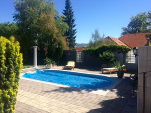 A swimming pool with a tiled deck, surrounded by potted plants and a wooden bench. - Ferienhaus Piešťany (Banka)
