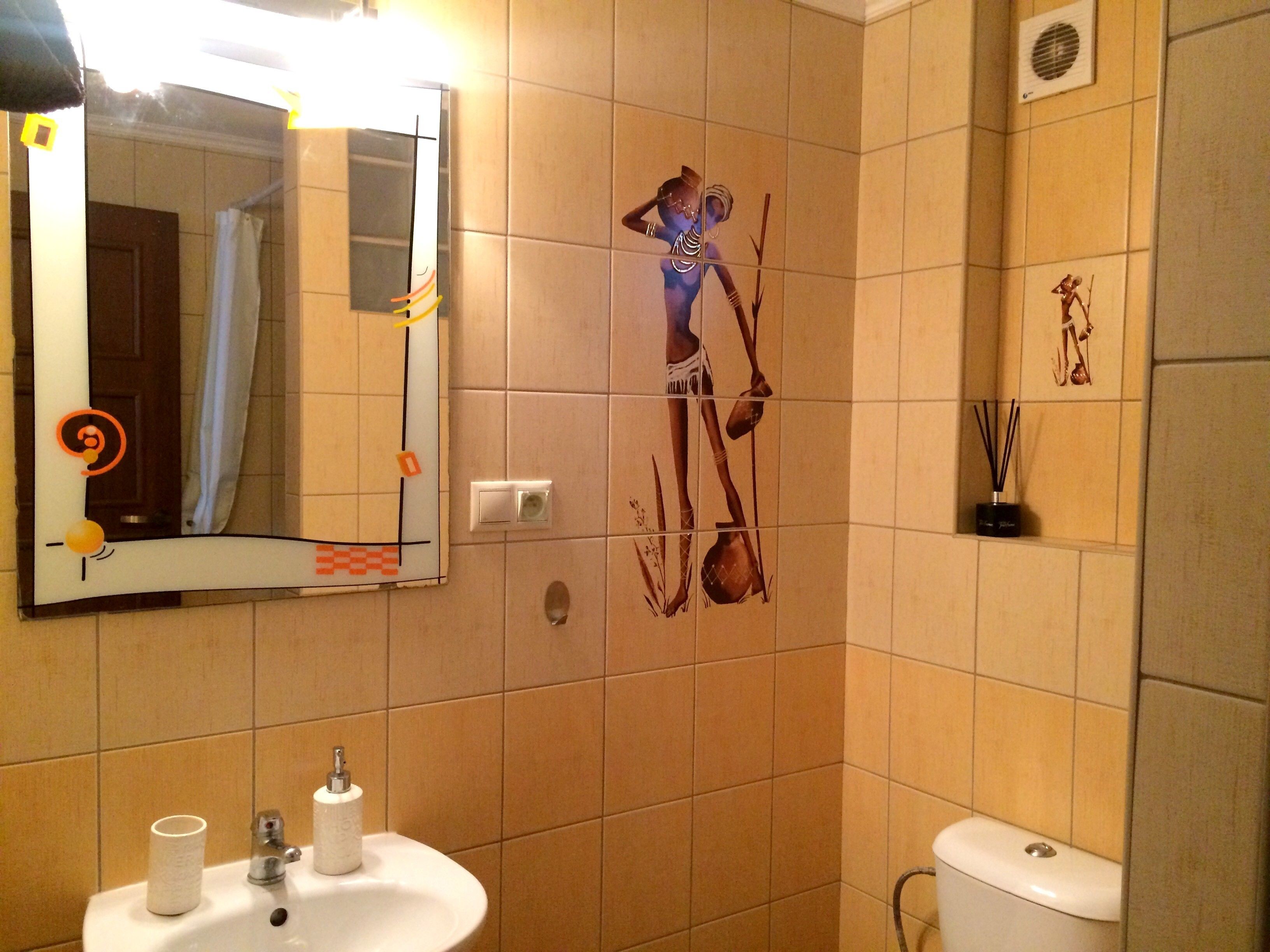 A bathroom with a sink, mirror, toilet, and decorative wall tiles.