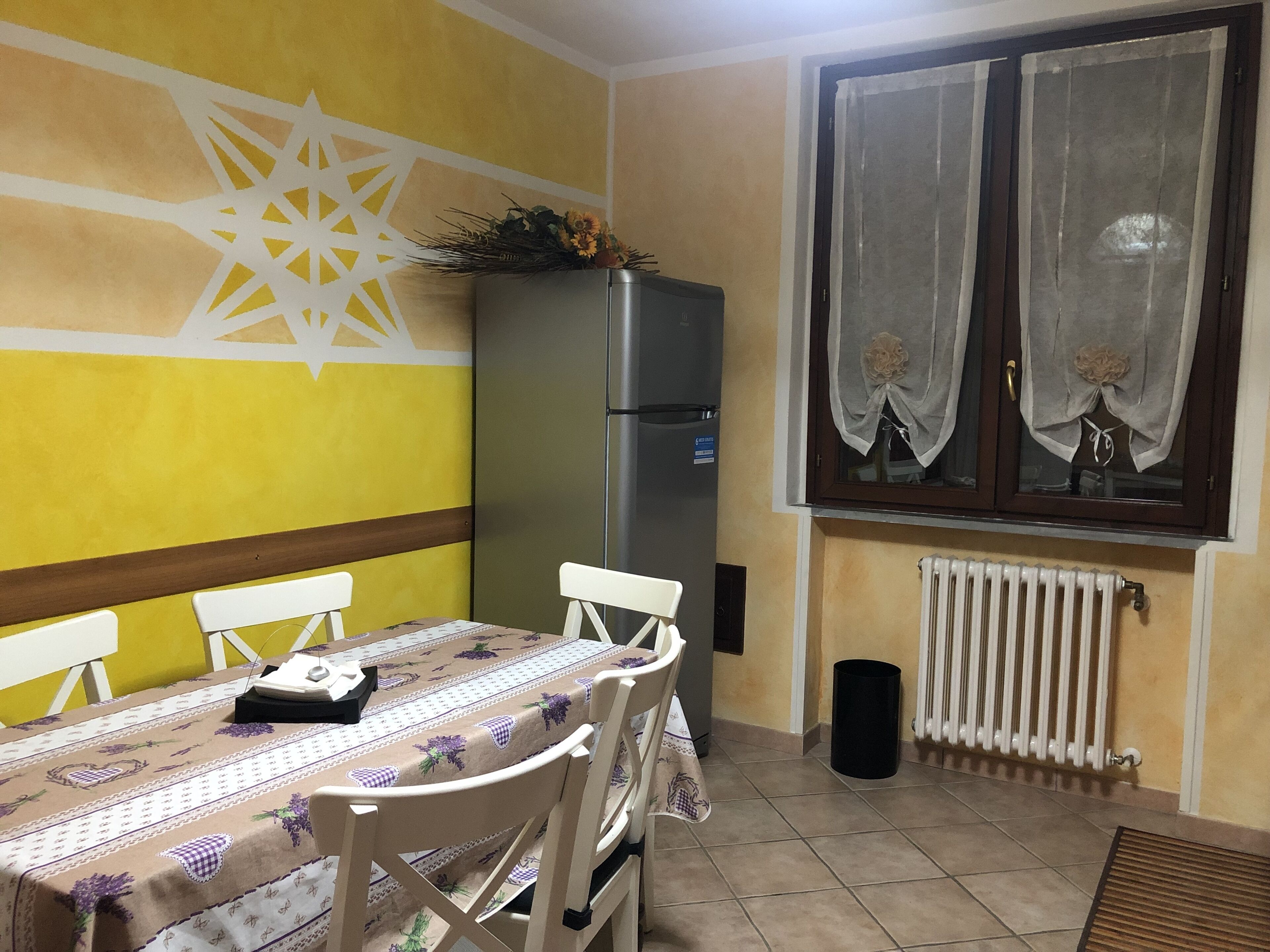 Un comedor con una mesa dispuesta para cuatro, un refrigerador y una ventana con cortinas.