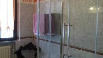 A bathroom with a glass-enclosed shower, a bathtub, a radiator, and a decorative wall piece.