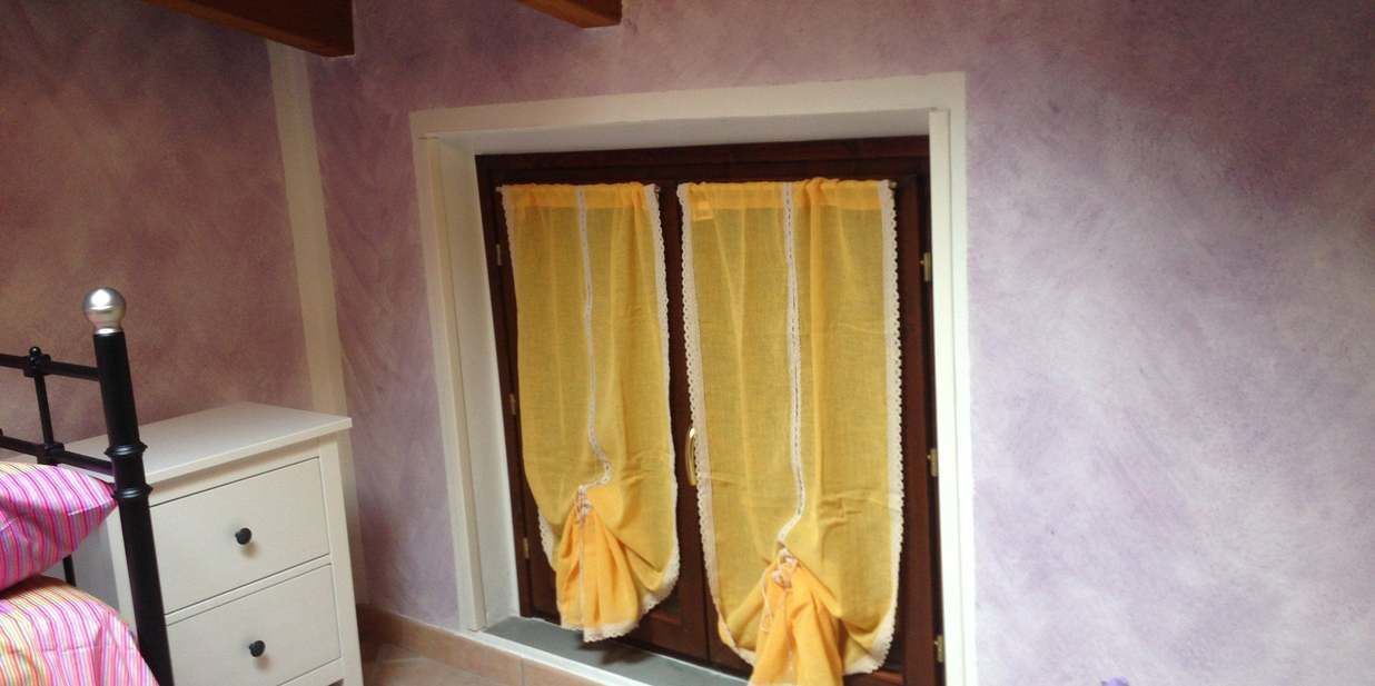 Una habitación con ventana cubierta por cortinas amarillas, un tocador blanco y una silla rosa.