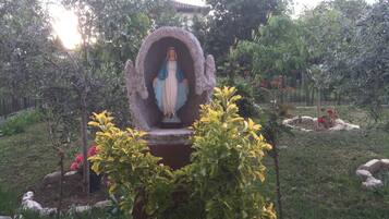 Una estatua de figura religiosa en un nicho rodeado de follaje y rocas.