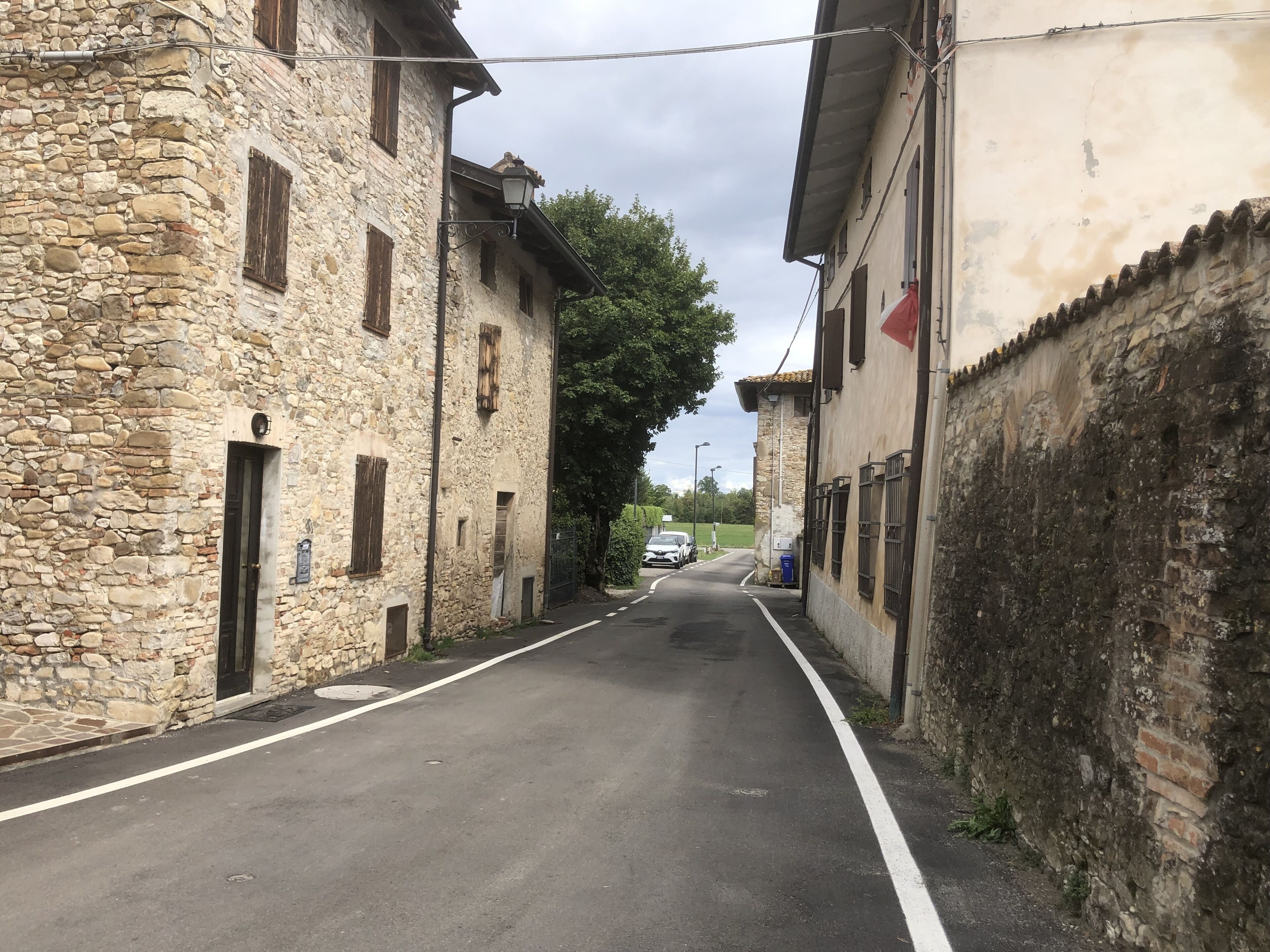A narrow street flanked by stone buildings with traditional architecture, a parked car, and a clear sky.