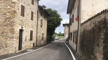 A narrow street flanked by stone buildings with traditional architecture, a parked car, and a clear sky.
