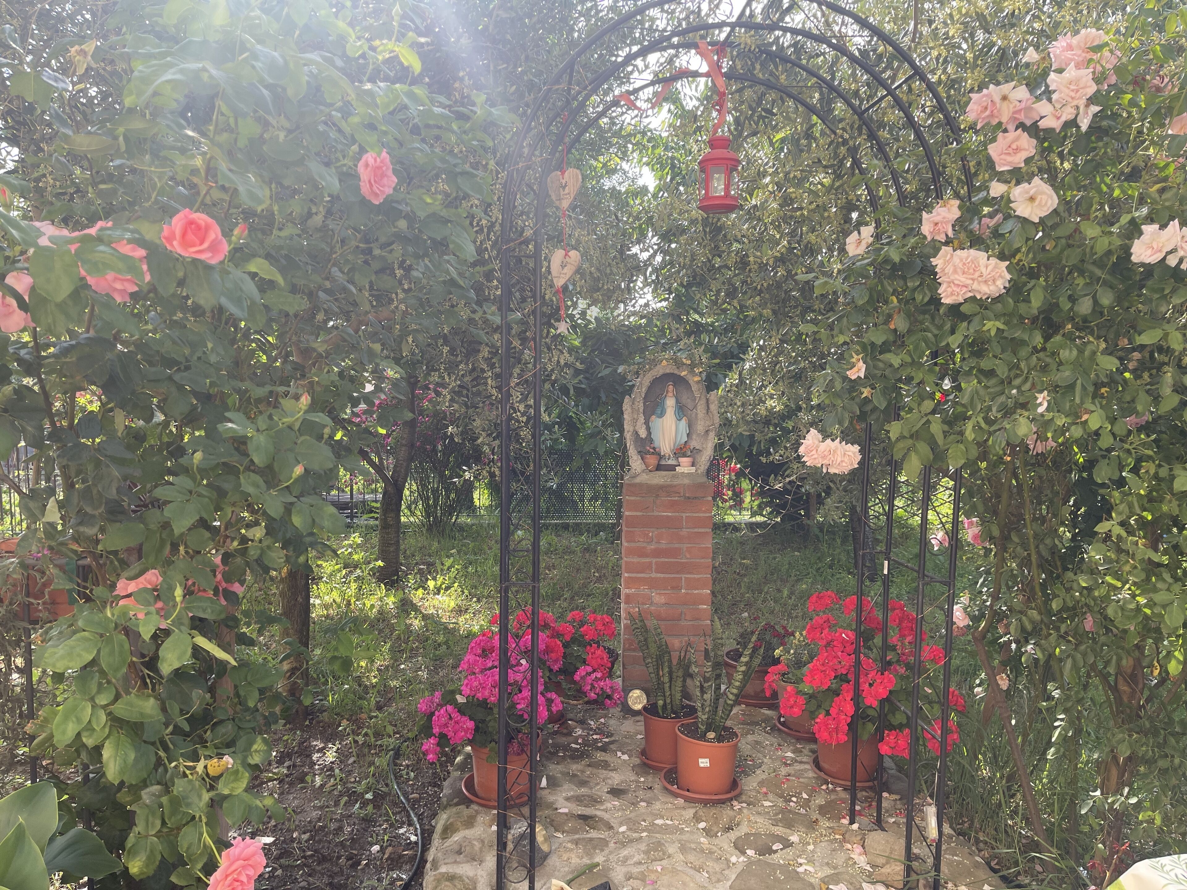Ein Garten mit einer Statue, Topfpflanzen und einem Metallbogen.