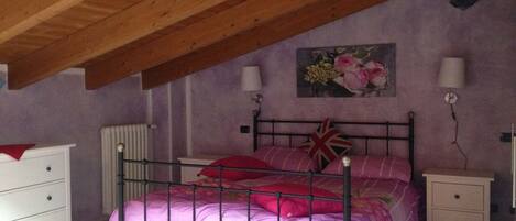 A bedroom with a sloped ceiling, a bed with pink bedding, two bedside tables with lamps, and a radiator.