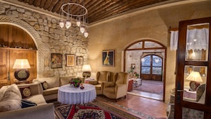Una habitación acogedora con paredes de piedra, techo de madera y un amplio arco que da al exterior. Hay una mesa redonda con mantel blanco, dos sillas y un sofá con cojines.