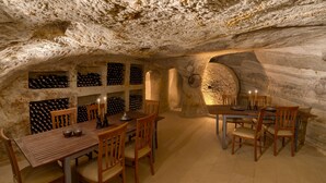 Una bodega con mesas y sillas de madera, estanterías para vino y una pared de piedra.