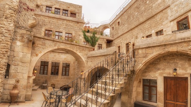 Un edificio de piedra con una escalera central, arcos de entrada y un pequeño espacio con mesa y sillas.
