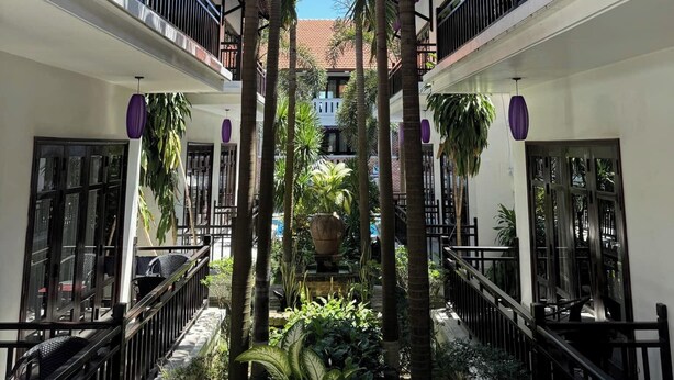 A courtyard with a central water feature, surrounded by tall palm trees and potted plants. - TTC Hotel – Hoi An (Da Nang)