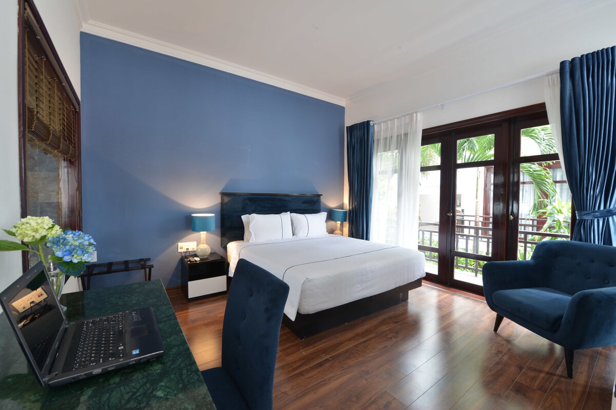 A hotel room with a bed, a desk with a laptop, a chair, and a view of the outdoors.