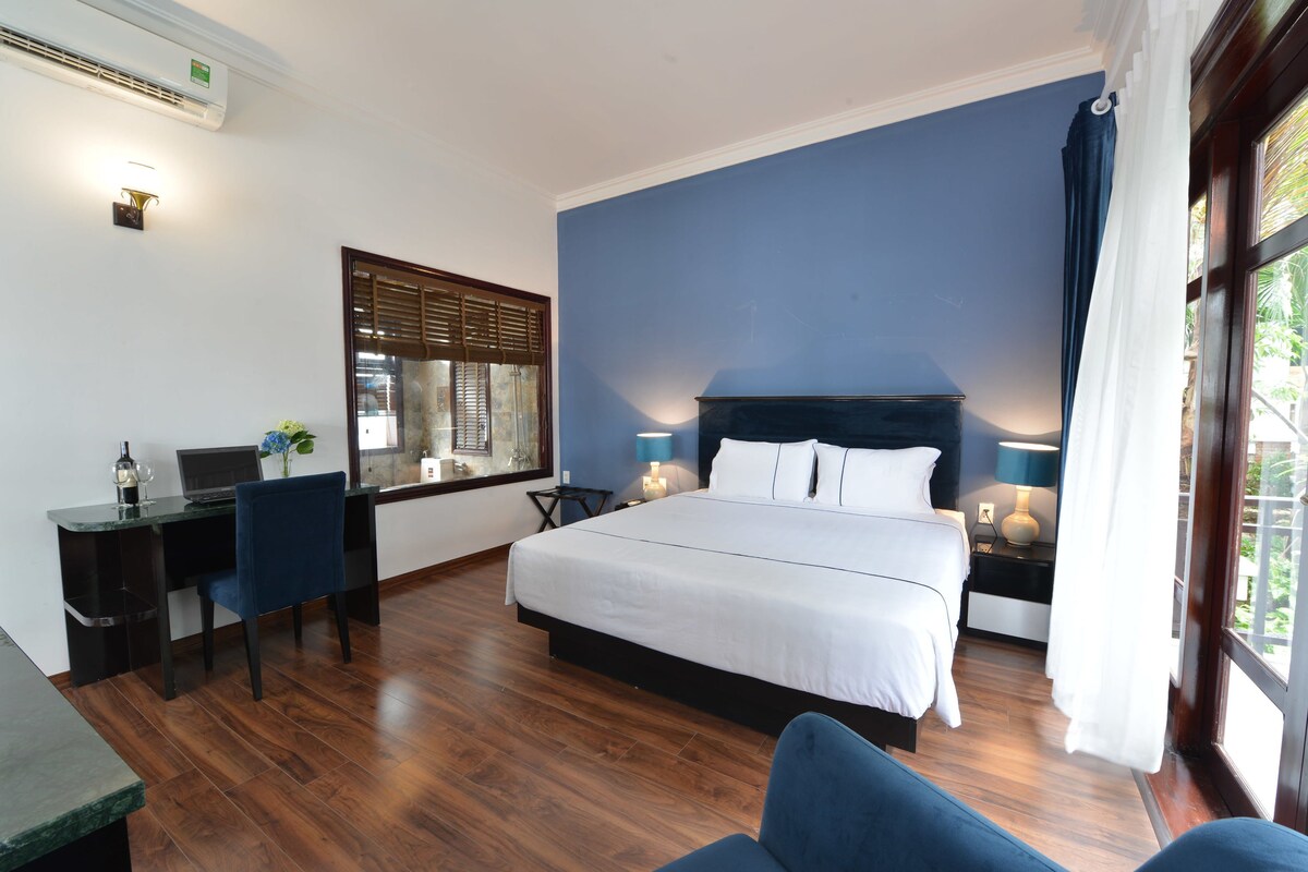 A bedroom with a bed, desk, chair, and a window with blinds.