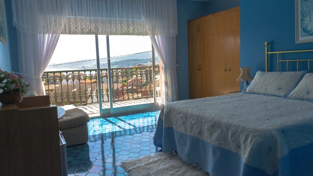 A bedroom with a bed, a wooden wardrobe, a window with a view of the outside, and a small balcony with a tiled floor. - Hotel Galicia (Poio)