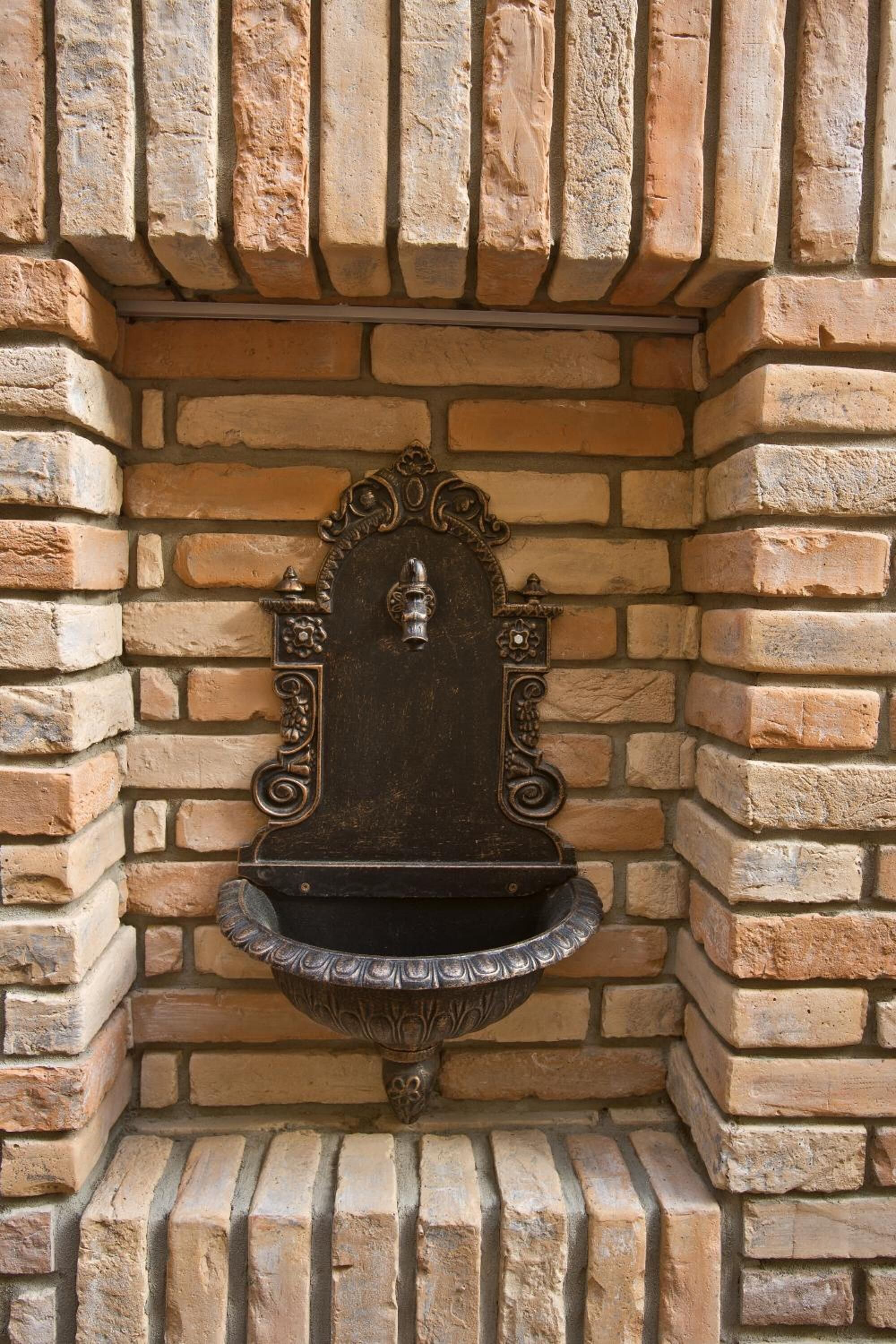 Un muro de piedra con una cuenca metálica decorativa.