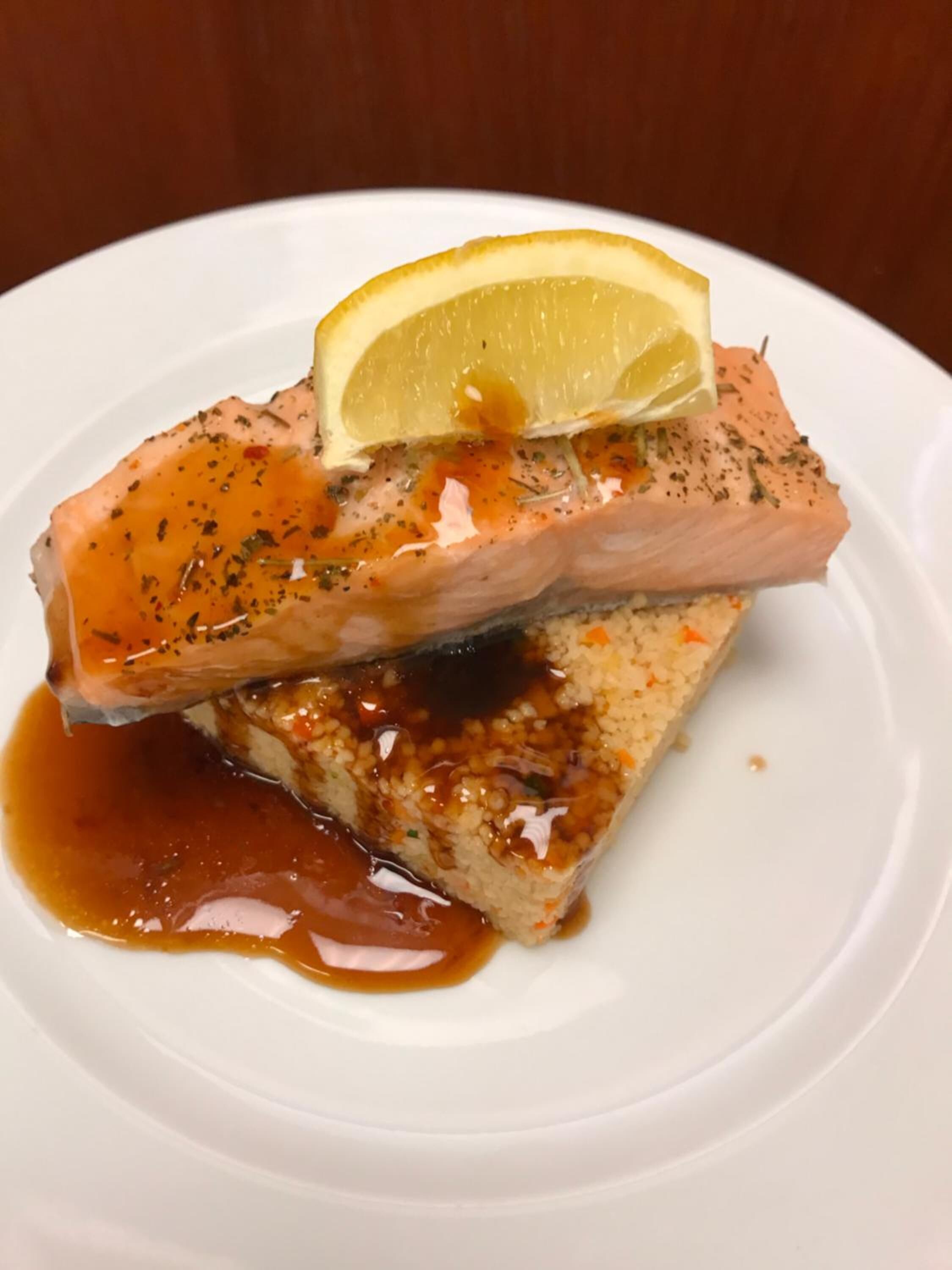 Une assiette contenant un morceau de saumon, garni d’une tranche de citron et nappé d’une sauce.