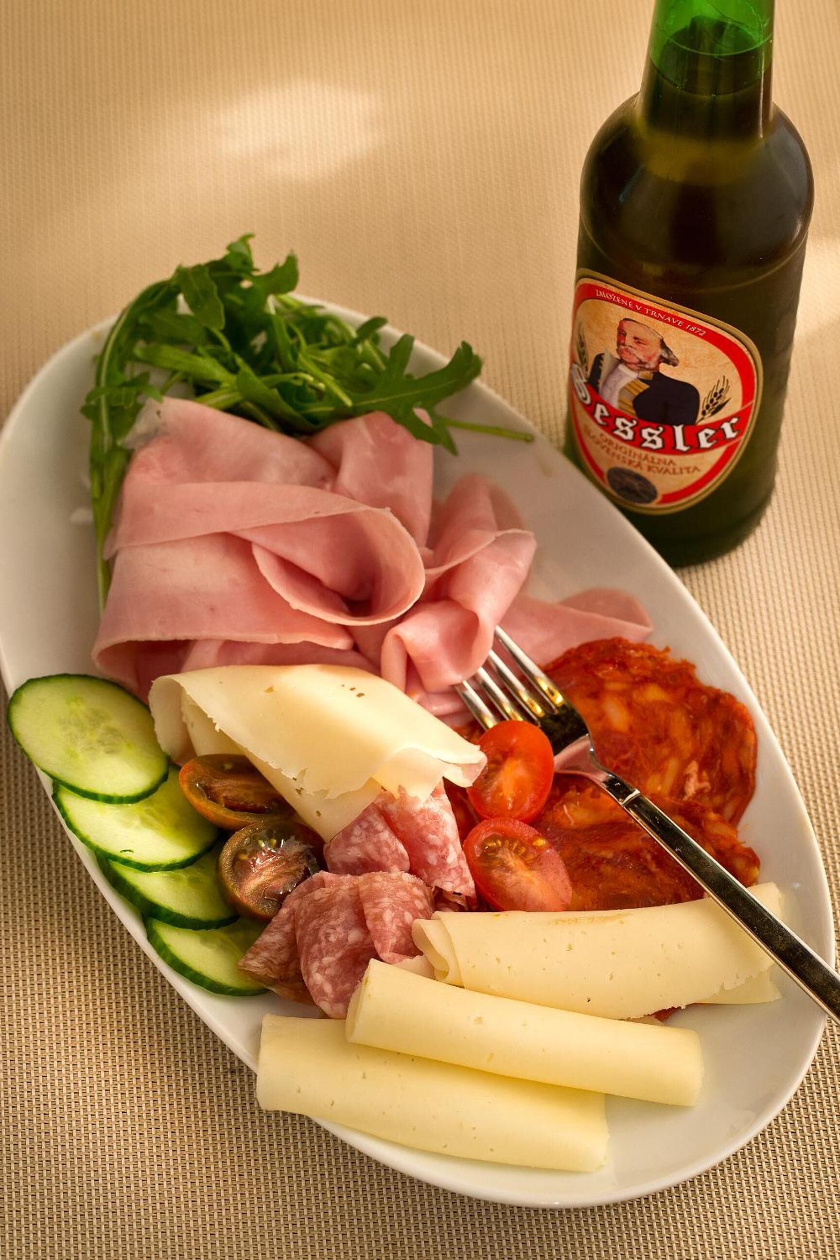 Un plato con diferentes carnes, queso y verduras, acompañado de una botella de cerveza Esslet.