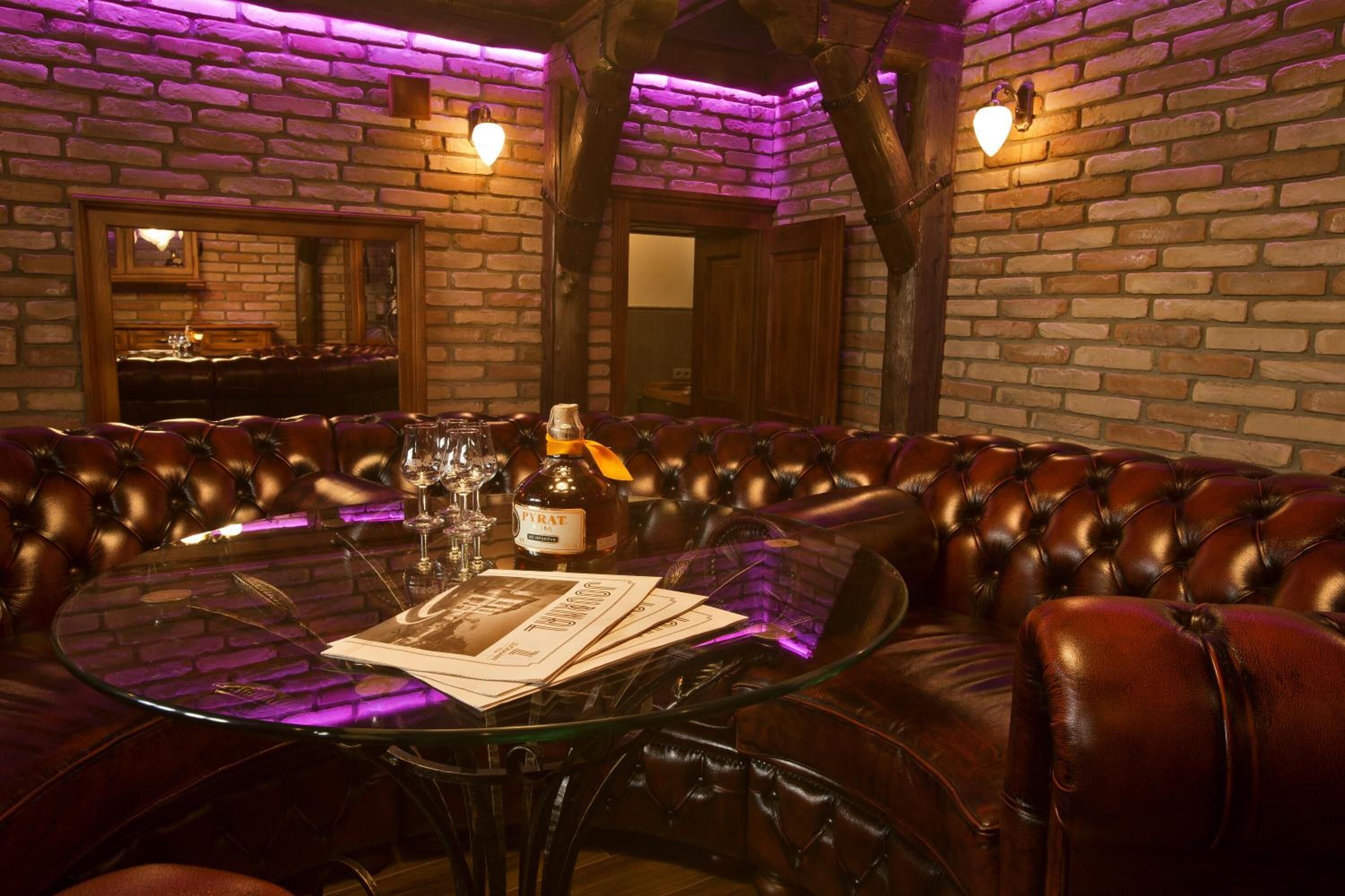 A round glass table with a bottle of Pirae wine, glasses, and menus in a leather booth seating area with brick walls and wooden beams.
