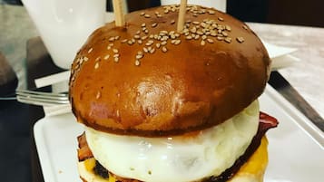 A sandwich with a sesame seed bun, cheese, bacon, and a fried egg, accompanied by fries and a small container of sauce.