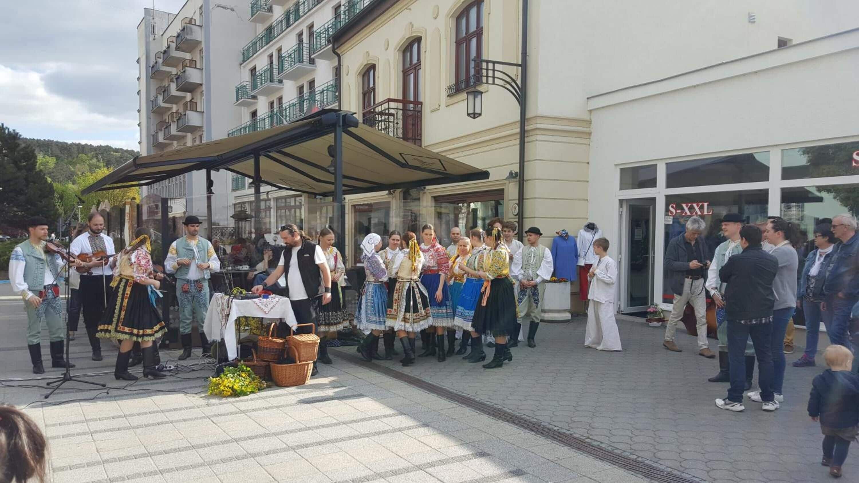 A group of people in traditional attire standing in front of a building with a sign reading "S XXL".