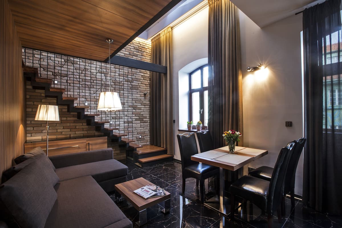 Un interior moderno con sofá, mesa de comedor y escalera frente a una pared de ladrillo.