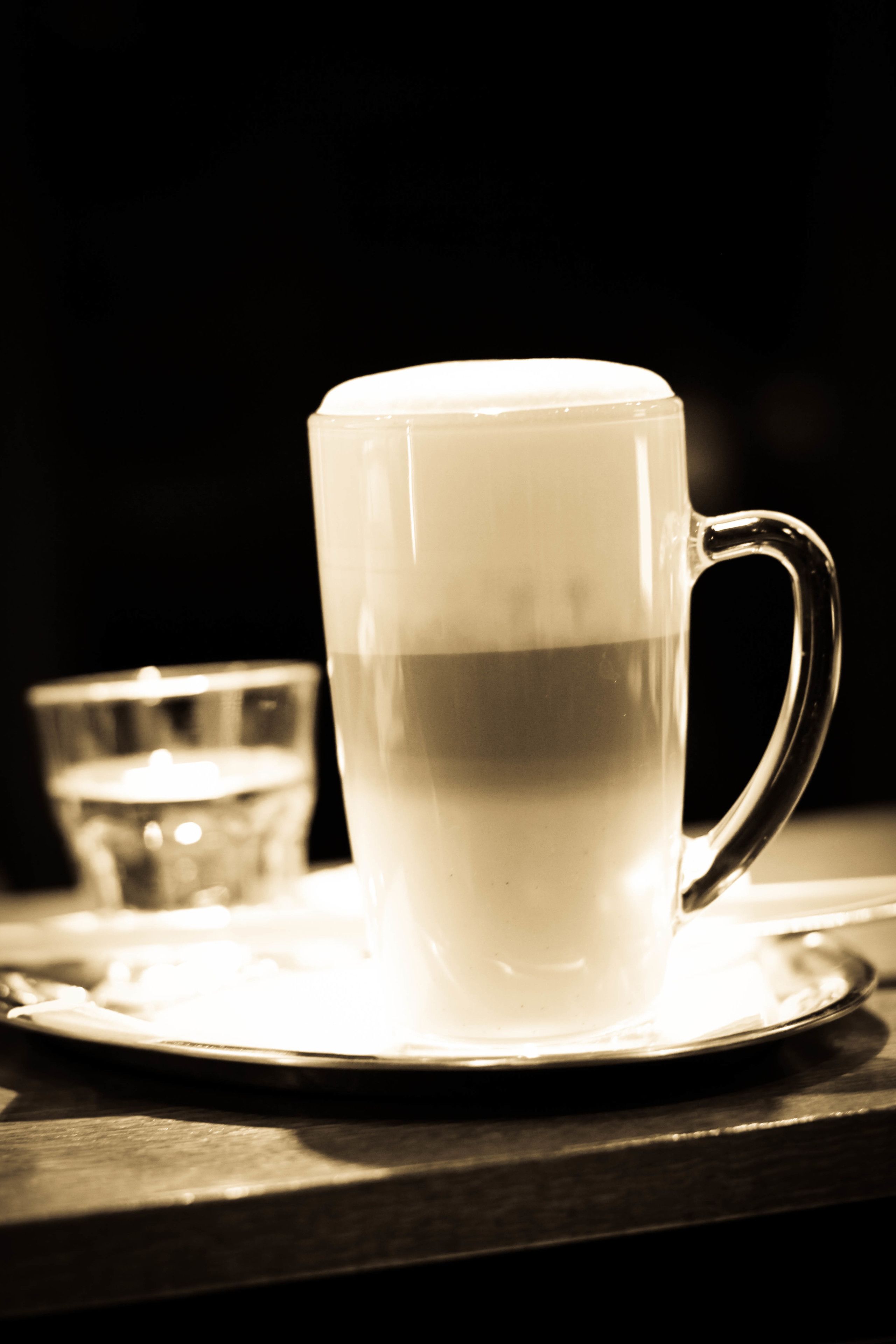 En genomskinlig glas mugg med handtag, placerad på en liten assiett som står på en träyta.