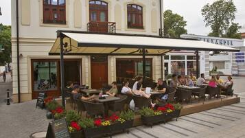 An outdoor cafe with tables and chairs, a building with a balcony, and a signboard.