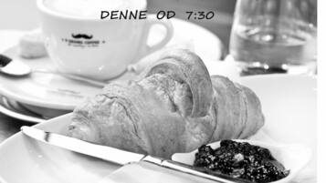 Un croissant sobre un plato con un cuchillo, una taza de café y un vaso de agua en una mesa.