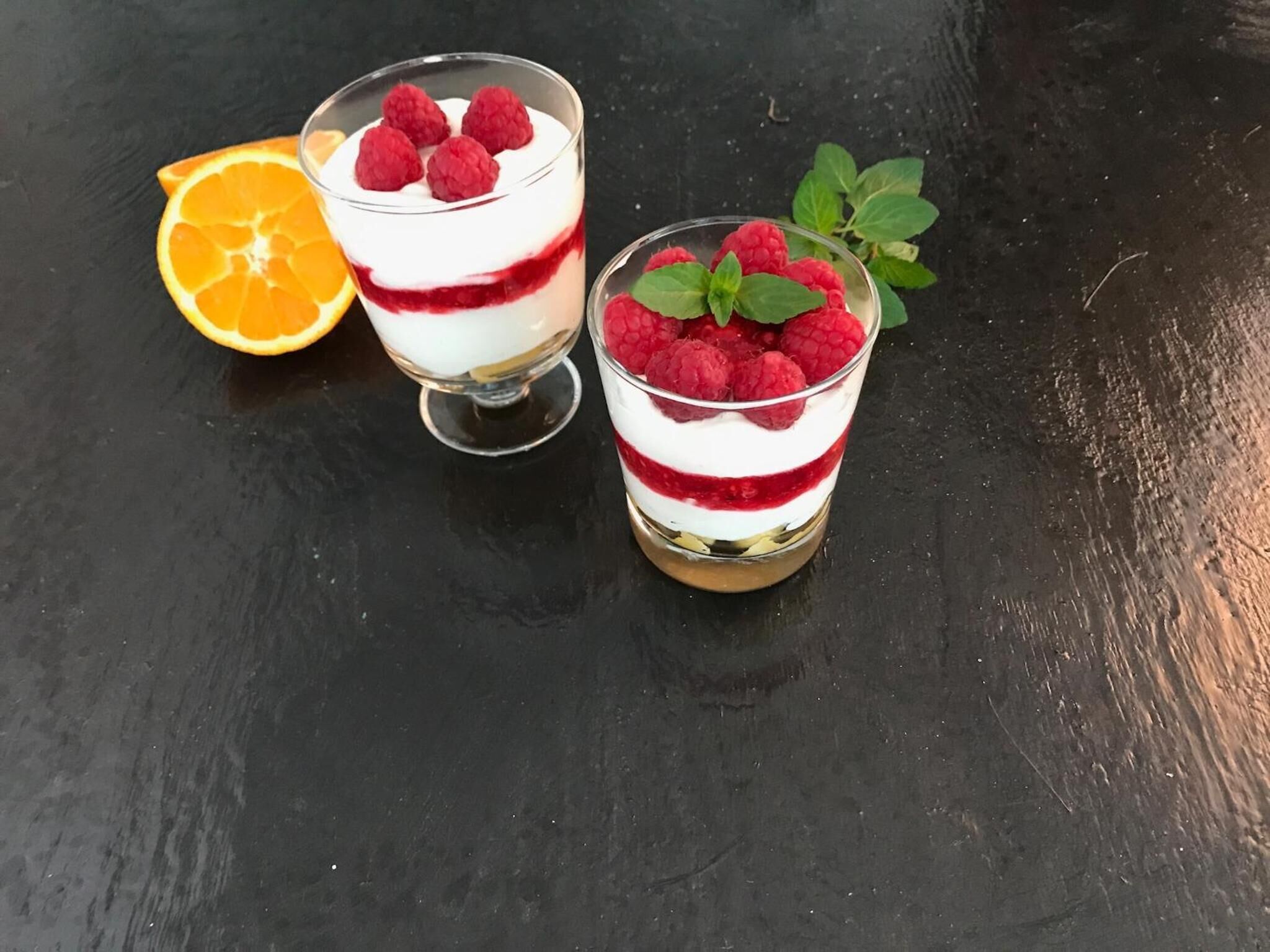 Two glasses of layered dessert with raspberries and mint leaves.