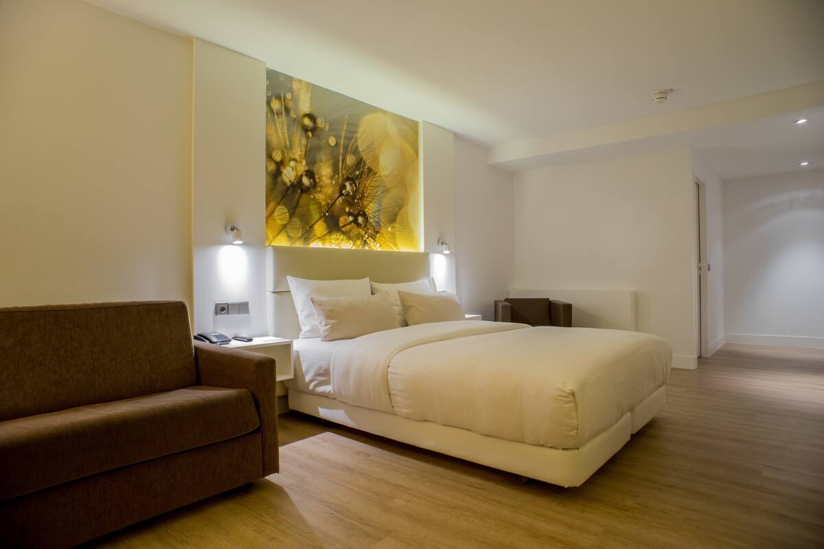 Ein modernes Hotelzimmer mit einem großen Bett, einer Couch und einem an der Wand befestigten Kunstwerk.