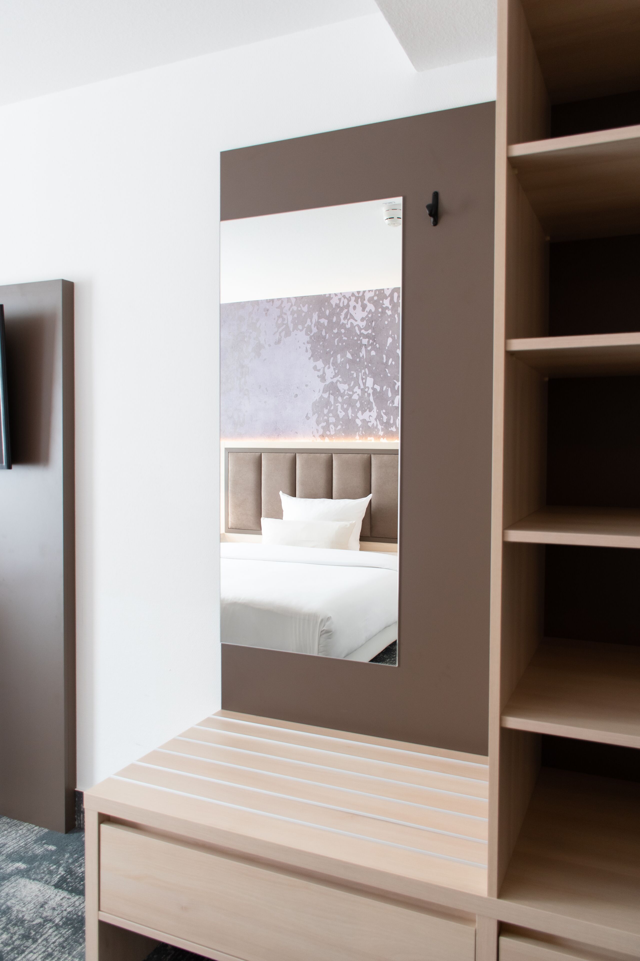 Una habitación de hotel moderna con una cama, una mesita de noche de madera y un espejo grande que refleja la habitación.