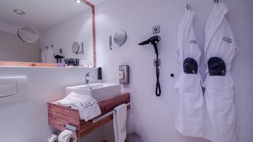 A modern bathroom with a wooden vanity, a mirror, a hairdryer, and two towels hanging on hooks.