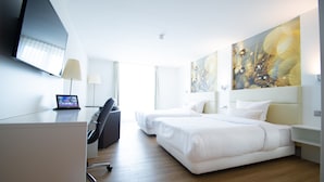 Une chambre d’hôtel équipée d’un bureau, de deux lits, d’une télévision et d’œuvres d’art accrochées aux murs.