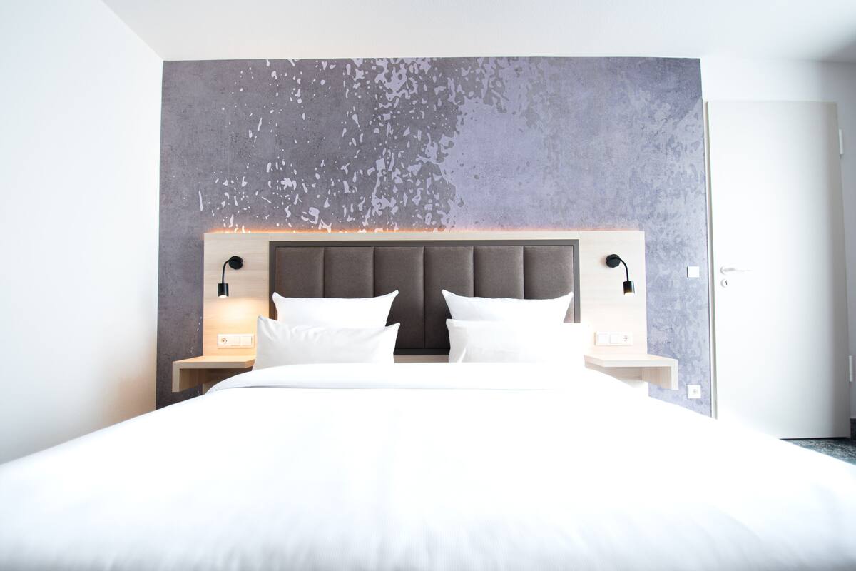 Ein modernes Hotelzimmer mit einem großen Bett, zwei Nachttischen mit Lampen und einer strukturierten Wand im Hintergrund.