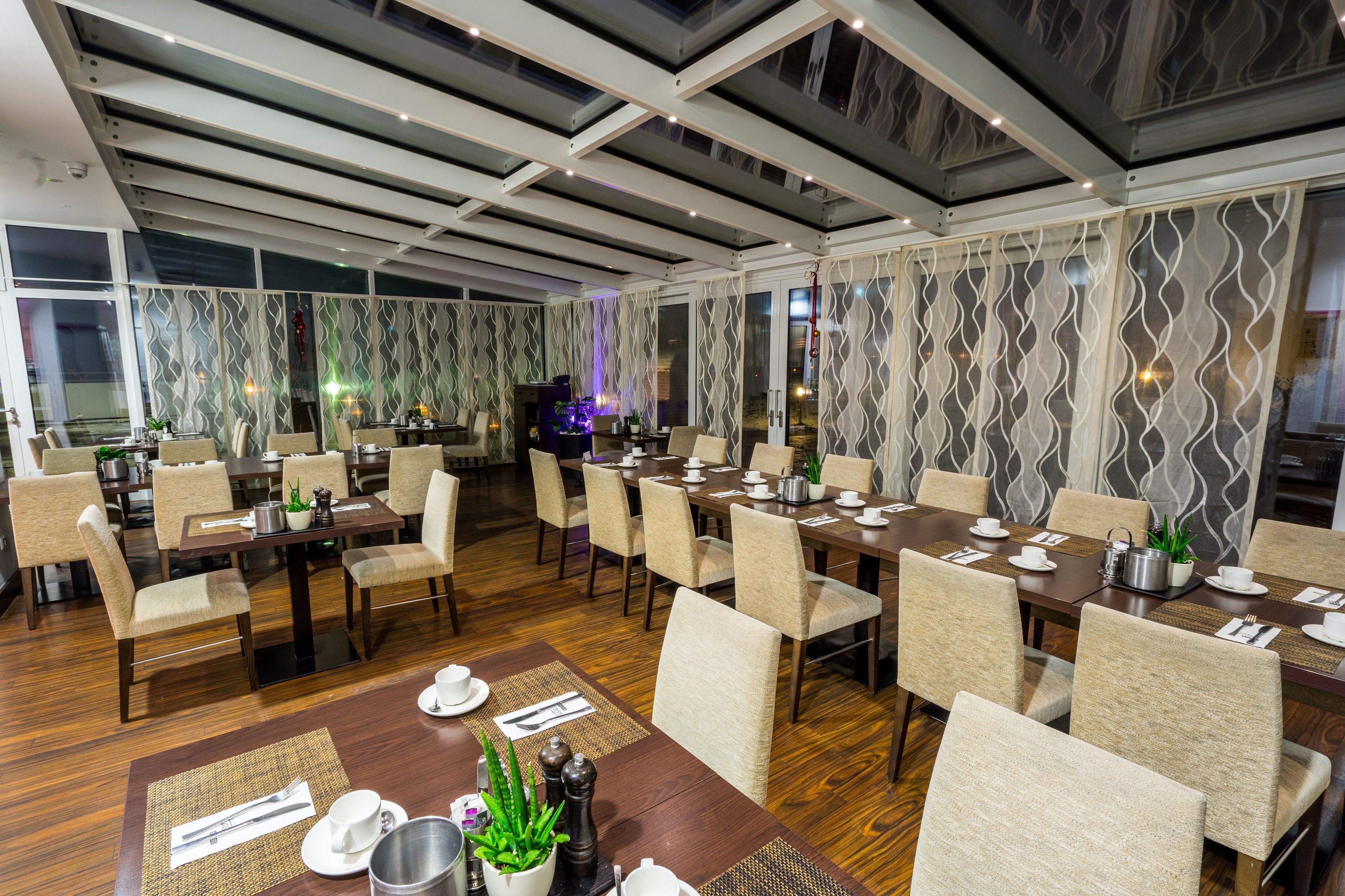 A dining area with multiple tables set for service, chairs arranged around them, and a decorative plant centerpiece.