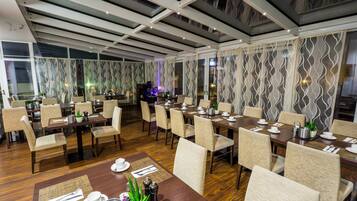 A dining area with multiple tables set for service, chairs arranged around them, and a decorative plant centerpiece.