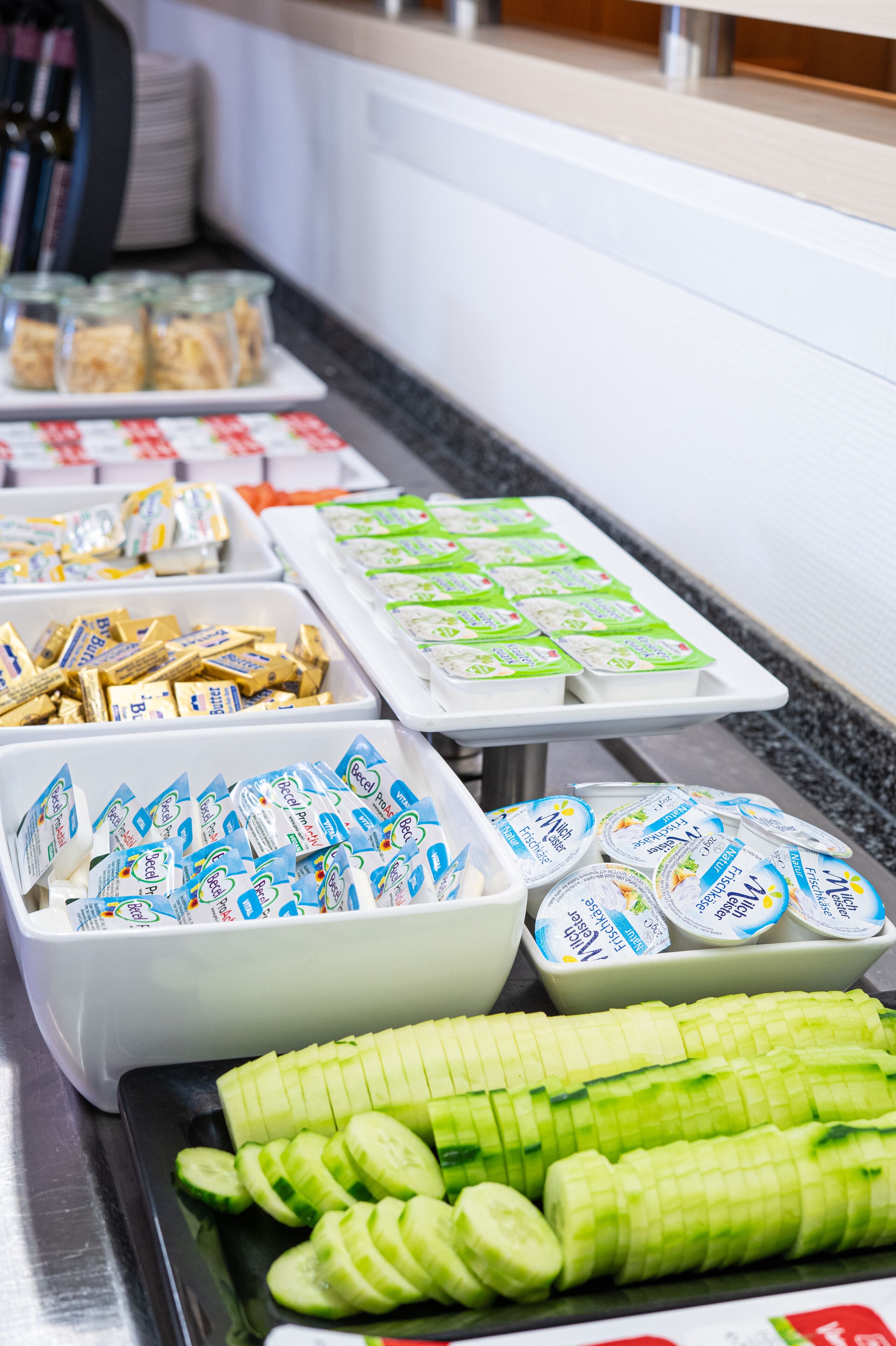Un bufé con diversos alimentos, incluyendo pepinos en rodajas, bocadillos empaquetados y productos lácteos.