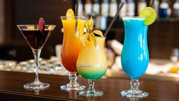 Three colorful drinks on a bar counter with a blurred background of bottles.
