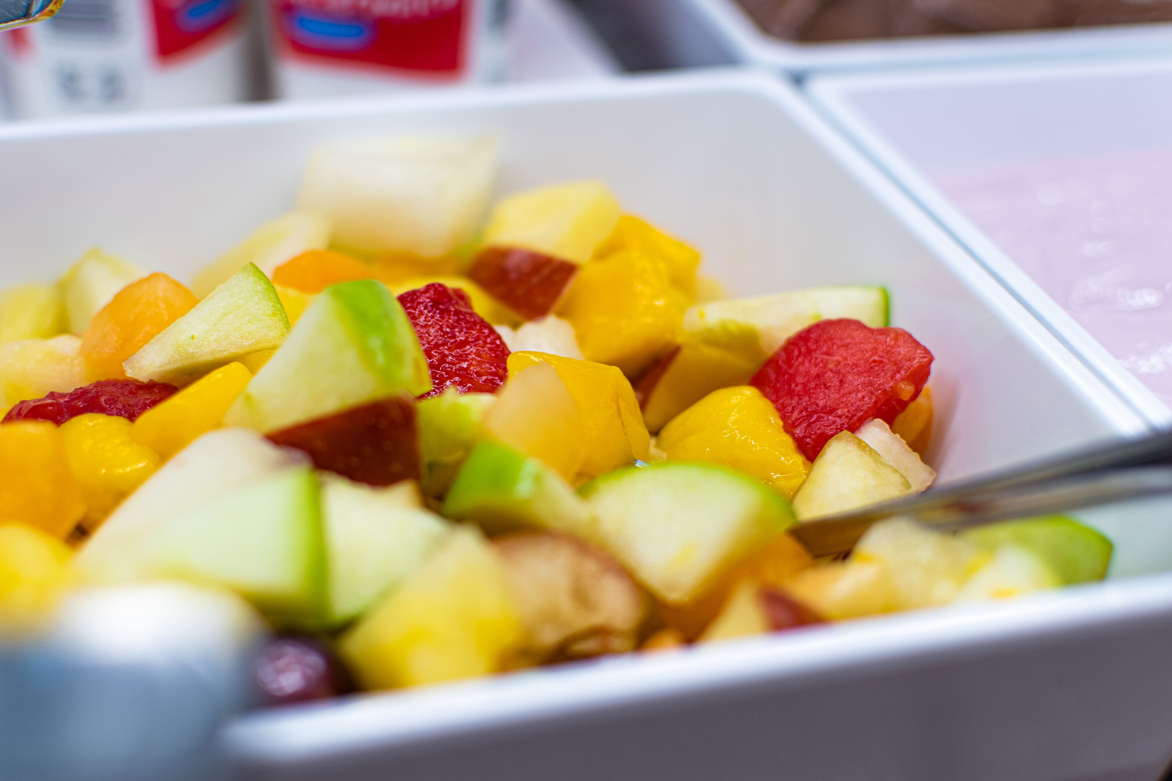 Un bol de salade de fruits composée de différents fruits, accompagné d’une cuillère.