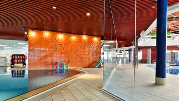 Una piscina interior con techo de madera, pared de vidrio y suelo de baldosas.