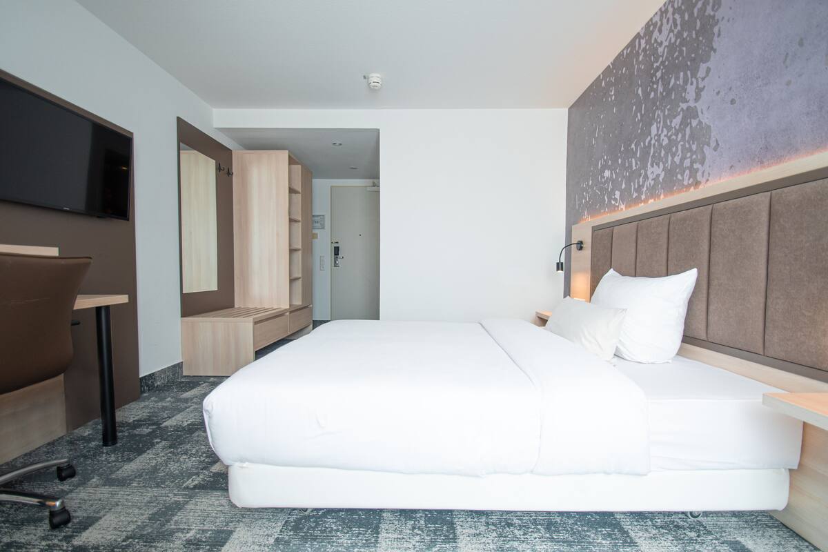 Ein modernes Hotelzimmer mit einem großen Bett, einem Schreibtisch und einem Fernseher.