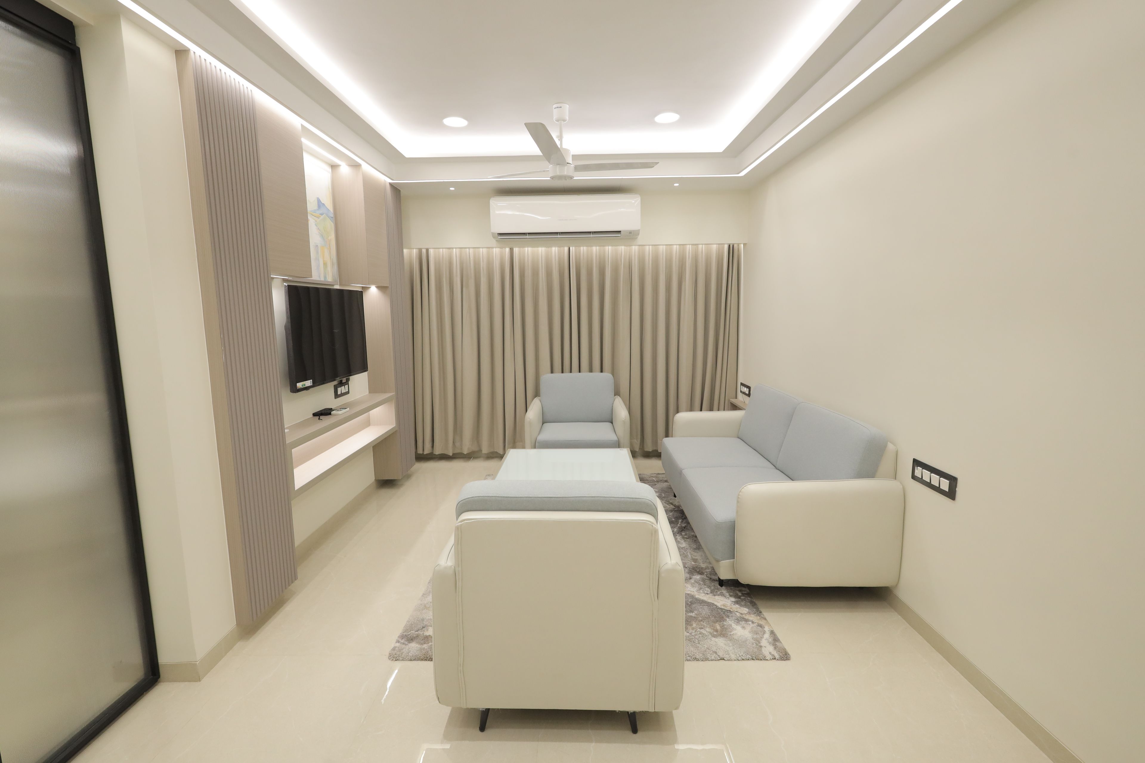 A modern living room with a flat-screen TV, a sofa, a coffee table, and a ceiling fan.