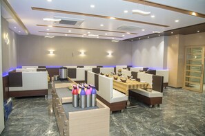 A modern hotel lobby with seating areas, a reception desk, and a buffet setup.