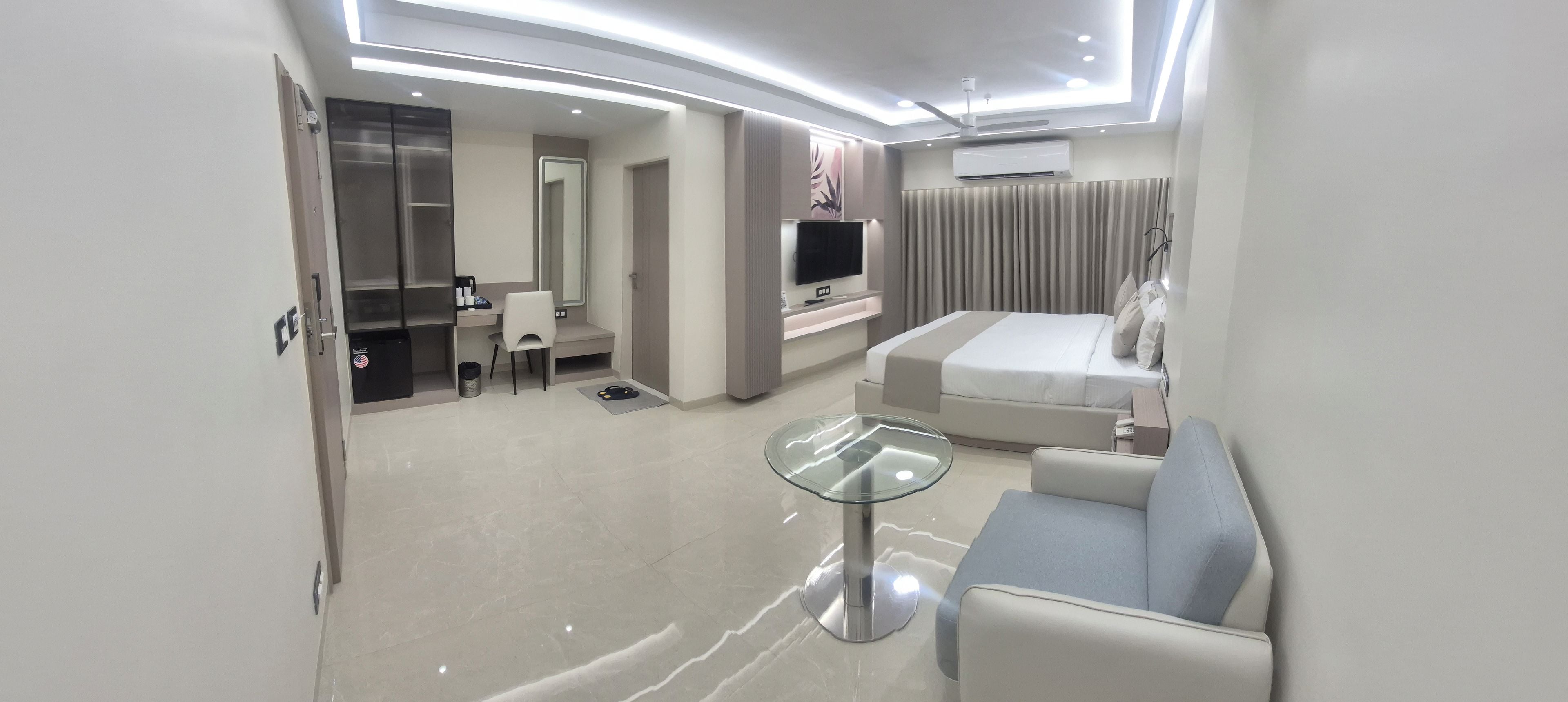 A modern hotel room with a bed, a TV, a sofa, a small table, and a desk with a chair.