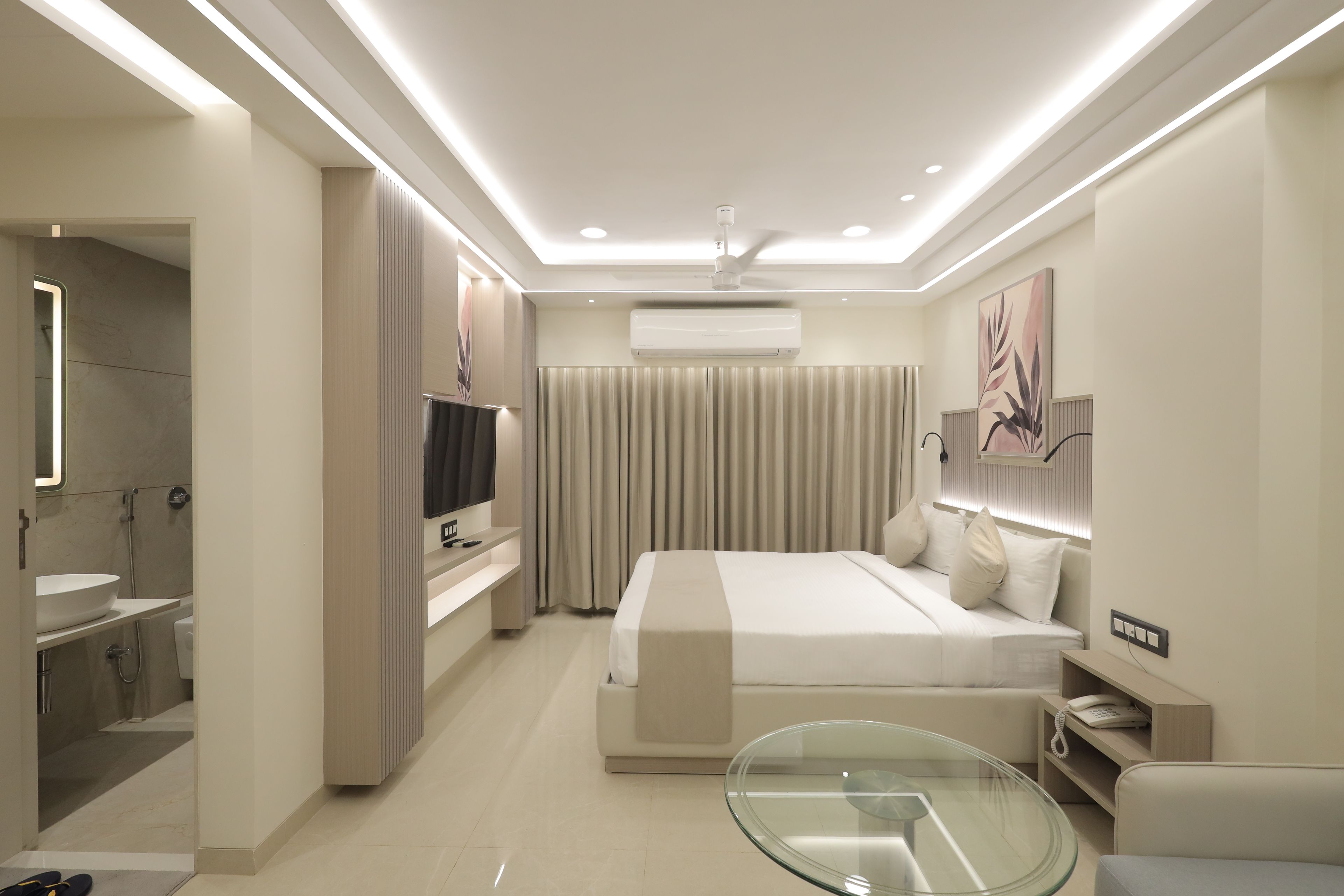 A modern hotel room with a bed, bedside table, TV, and a glass table.